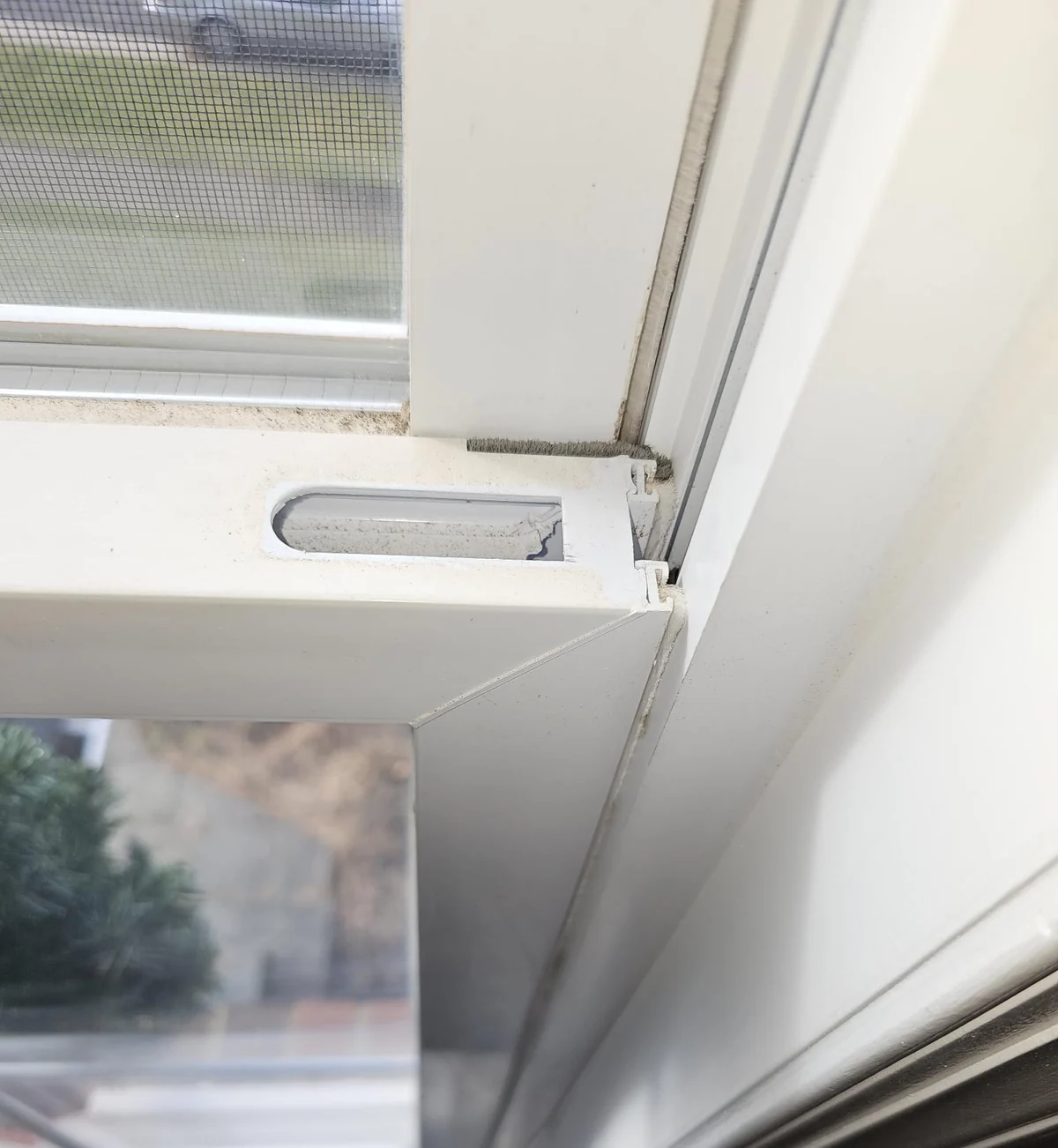 Damaged tilt latch at the top corner of a white window sash.