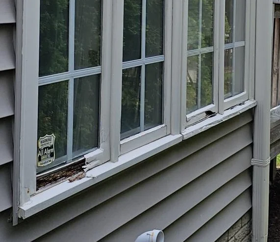 Exterior window frame with peeling paint and decayed wood along the lower sill.
