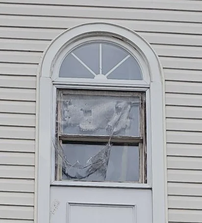 Storm door with torn screen mesh beneath a semicircular top window.