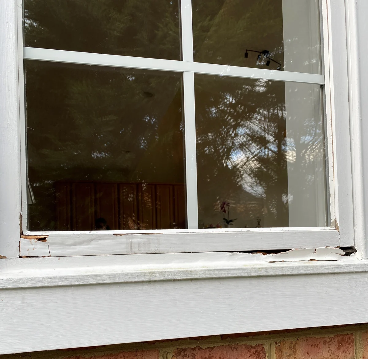 Weathered wooden window frame with cracked paint and damaged wood along the bottom.