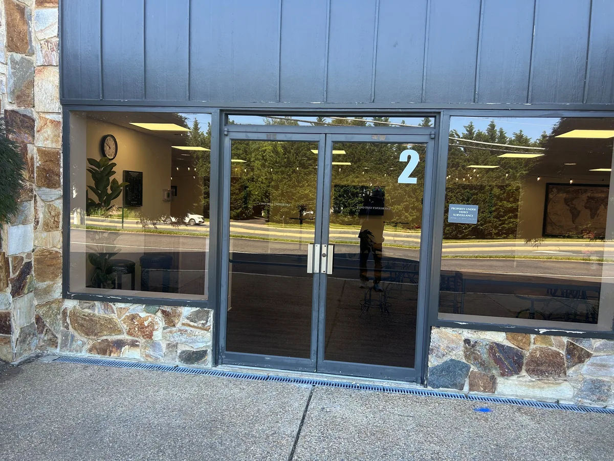 Dark-framed double glass storefront doors and windows with stone cladding below.