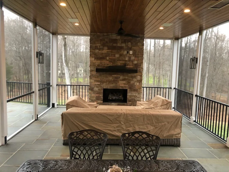 Screened porch with a wood ceiling, seating and a stone fireplace