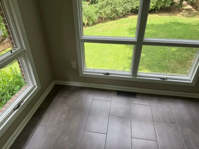 White corner windows overlooking a lawn in a tiled sunroom.