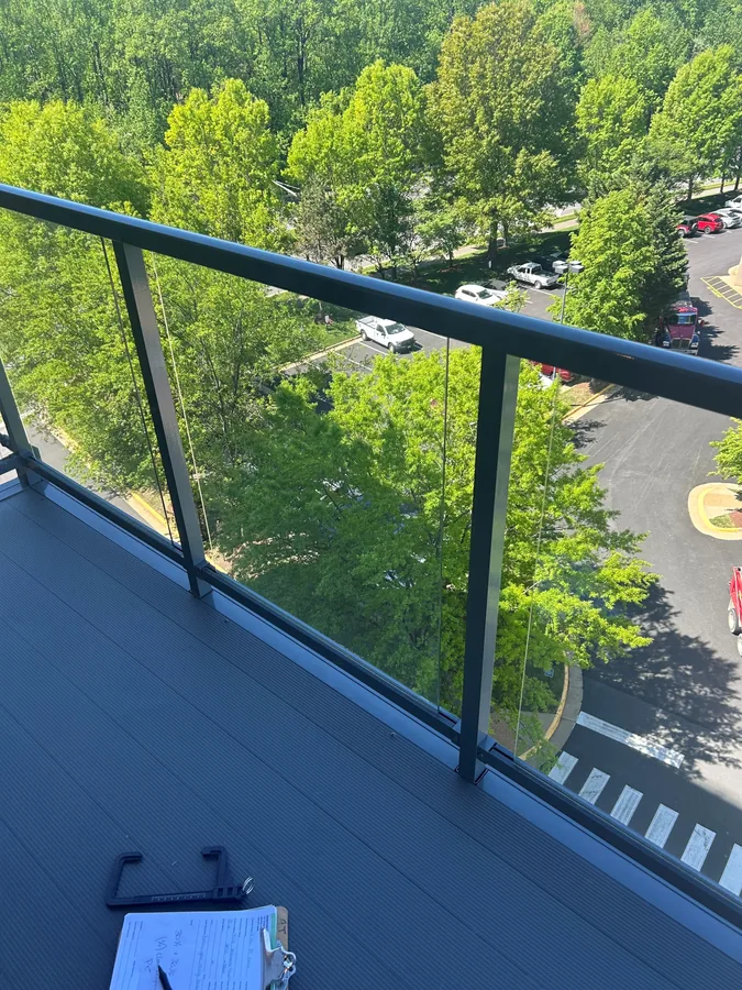 Clear glass balcony railing with dark metal posts overlooking trees.