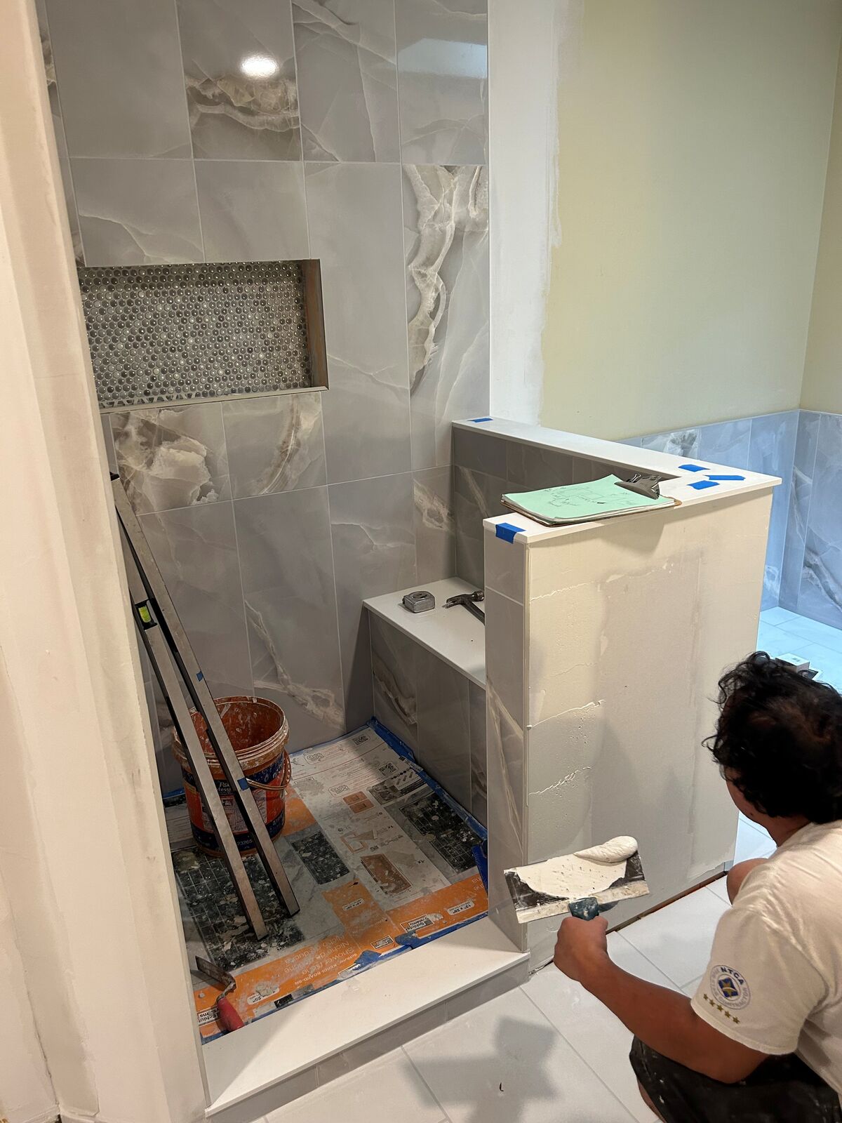 An installer working beside a finished tiled shower opening