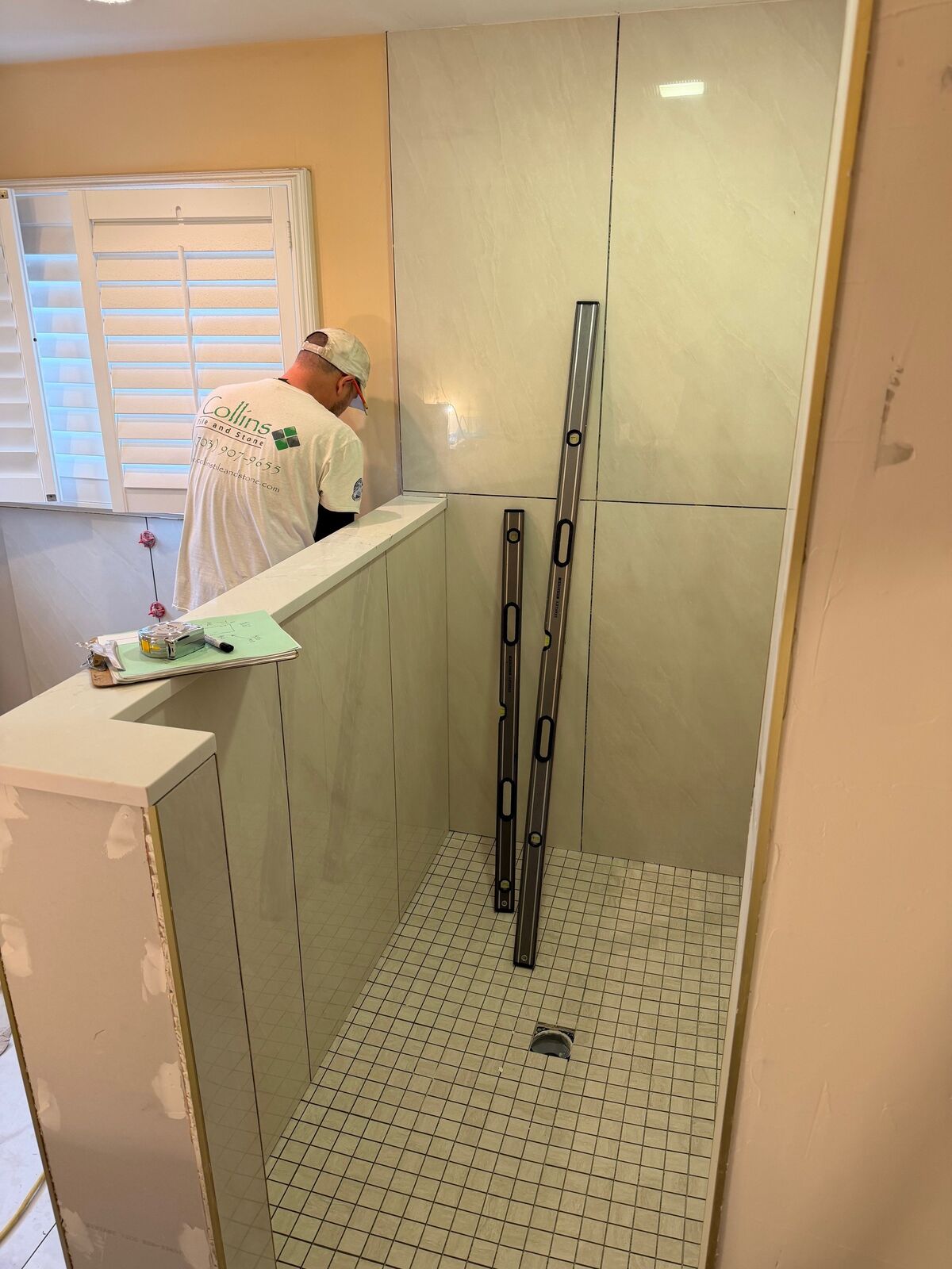 A tall glass shower panel set on a half wall, with levels in place during installation