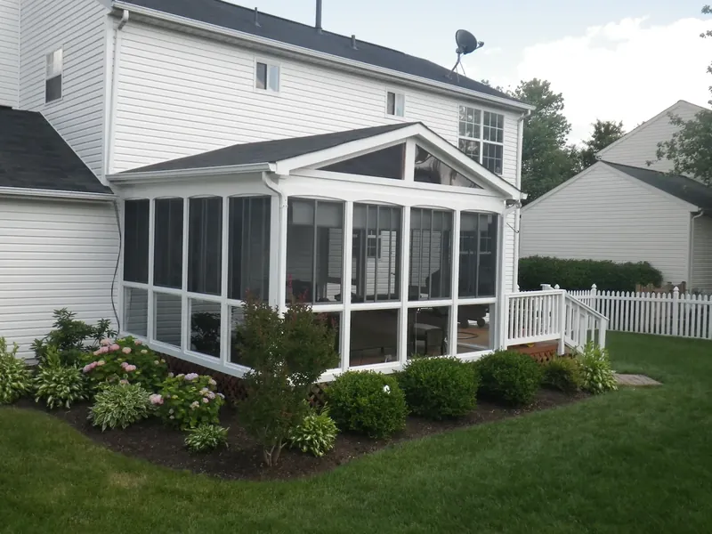 White gabled porch enclosure beside a landscaped lawn.