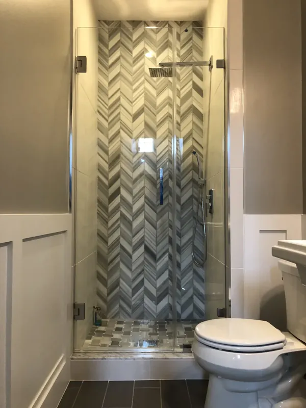 Narrow glass shower with chevron-pattern tile.