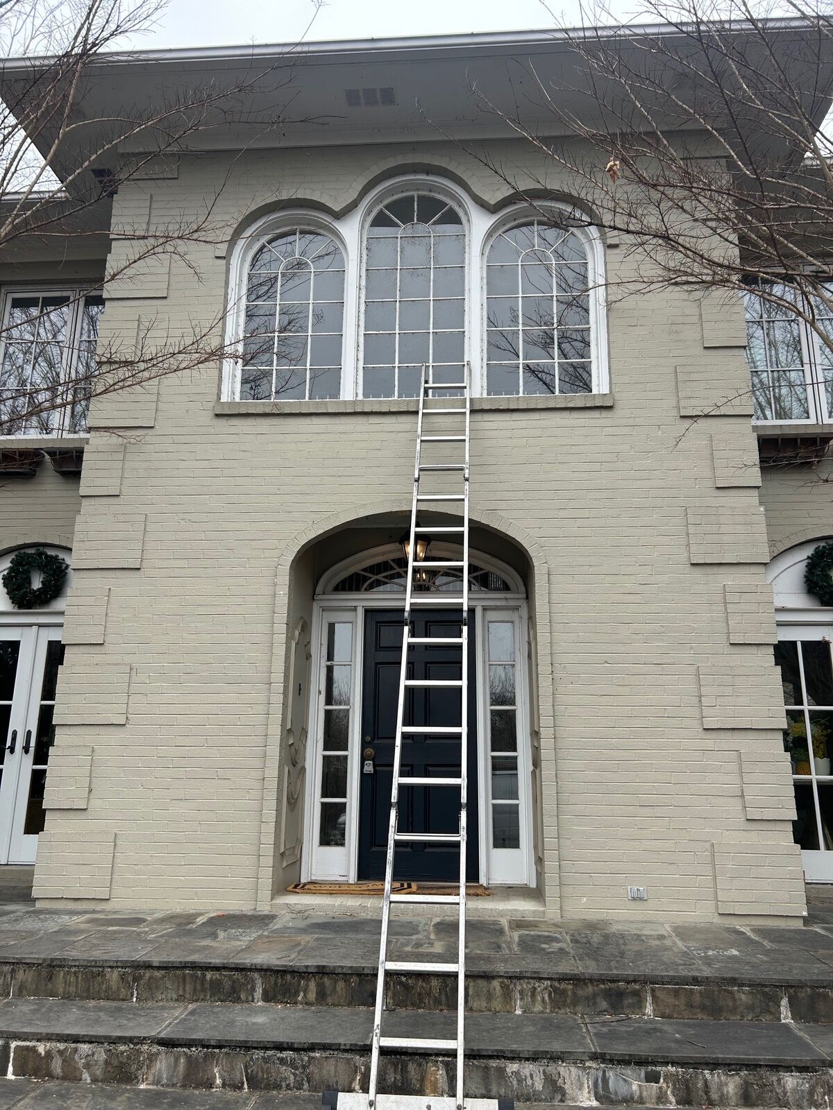 An extension ladder reaching arched upper-story windows on the outside of a home