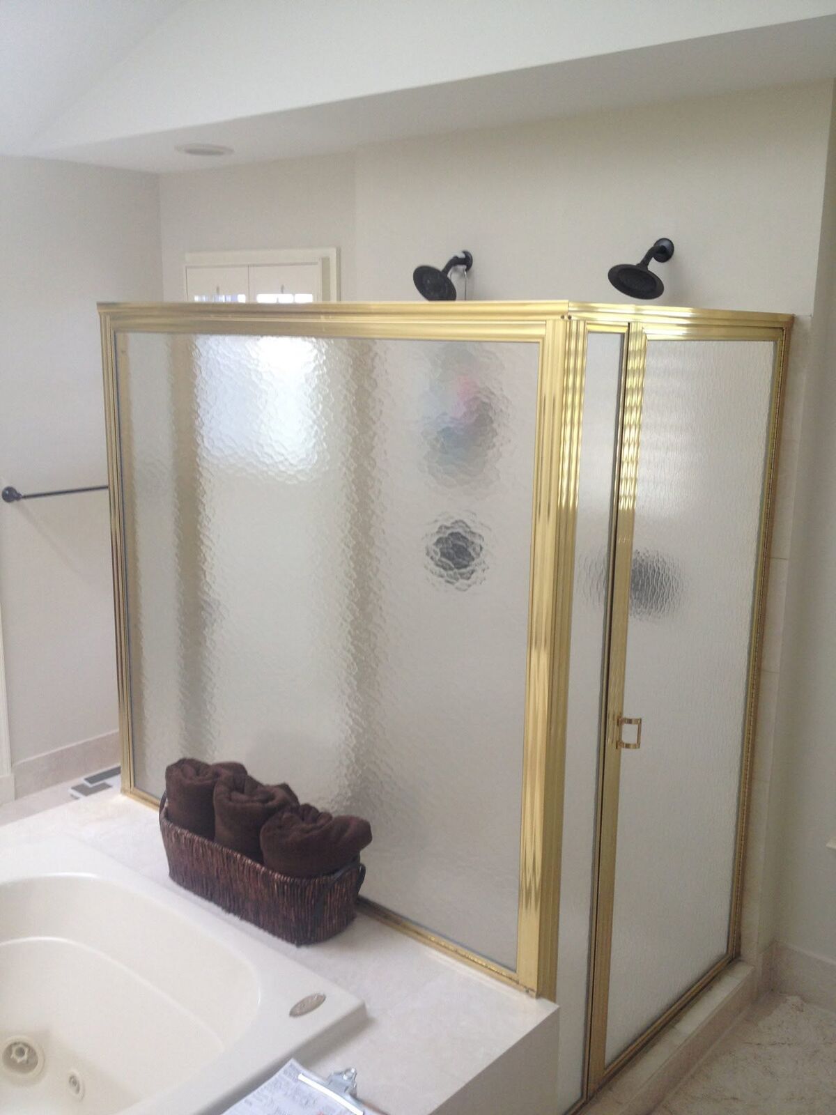 A gold-framed shower enclosure with patterned frosted glass beside a jetted tub