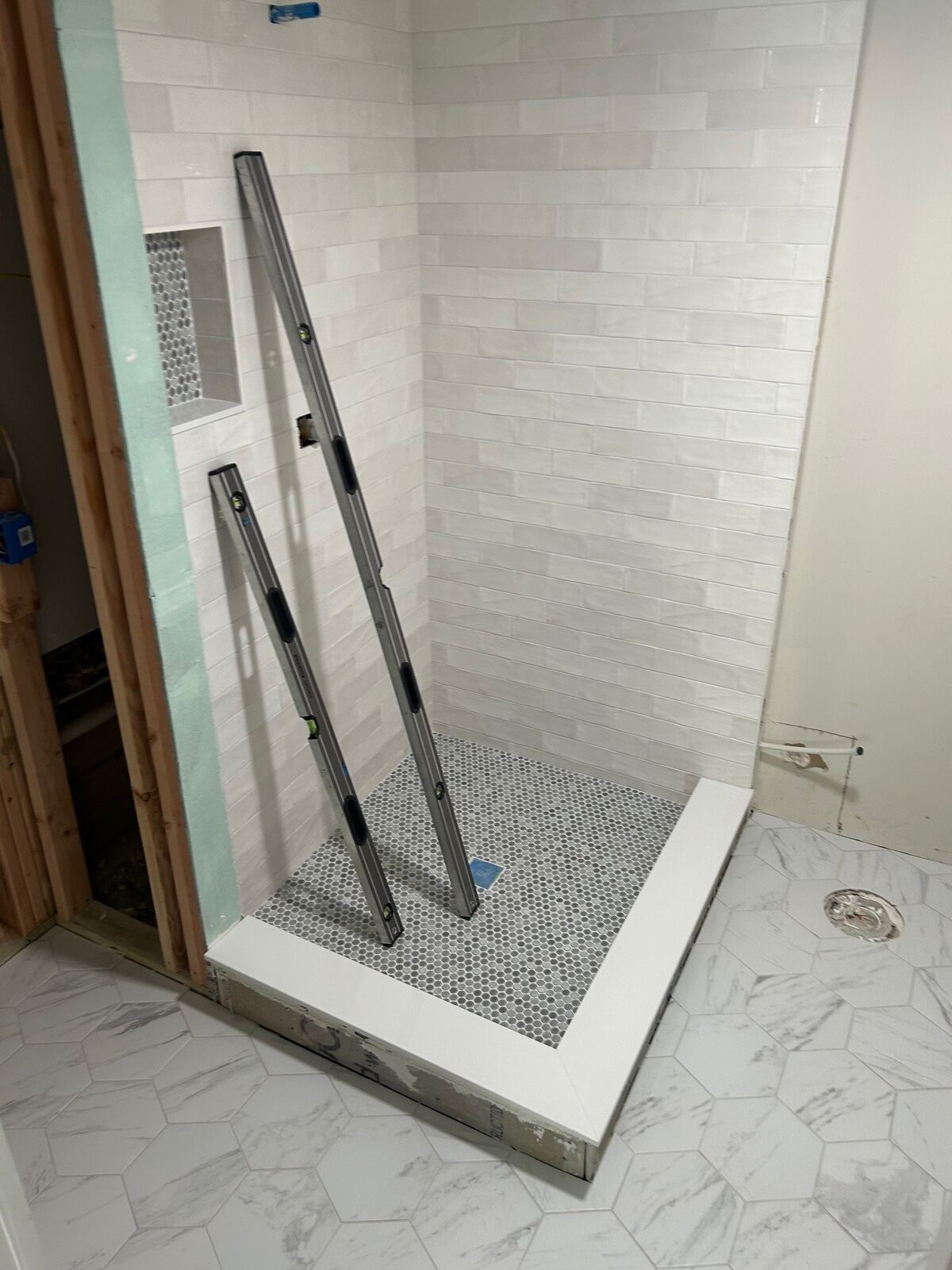 A narrow tiled shower opening with levels and measuring tools set up inside