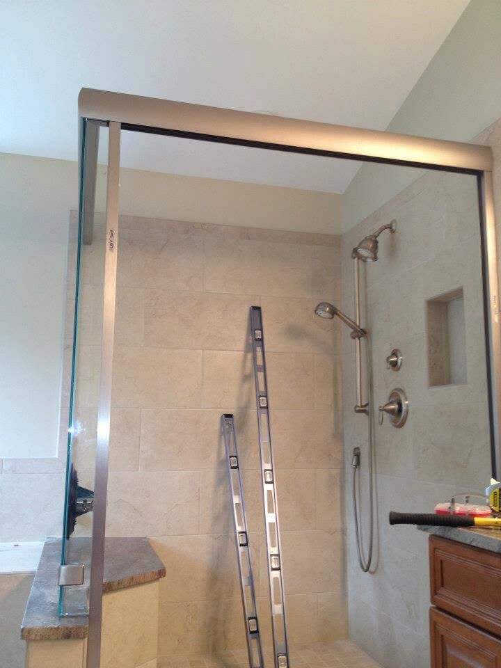 A glass shower enclosure being installed, with a ladder and tools inside the finished tile shower