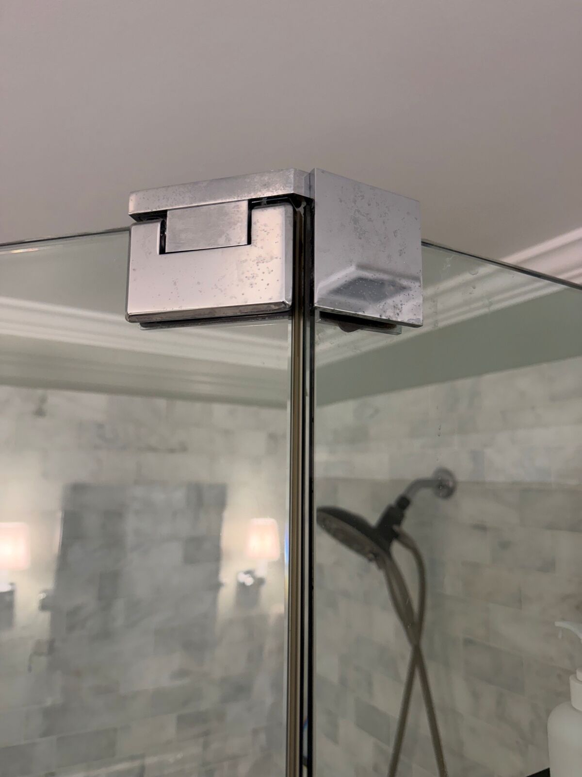 Close-up of the fitting that joins two frameless shower glass panels at the top corner