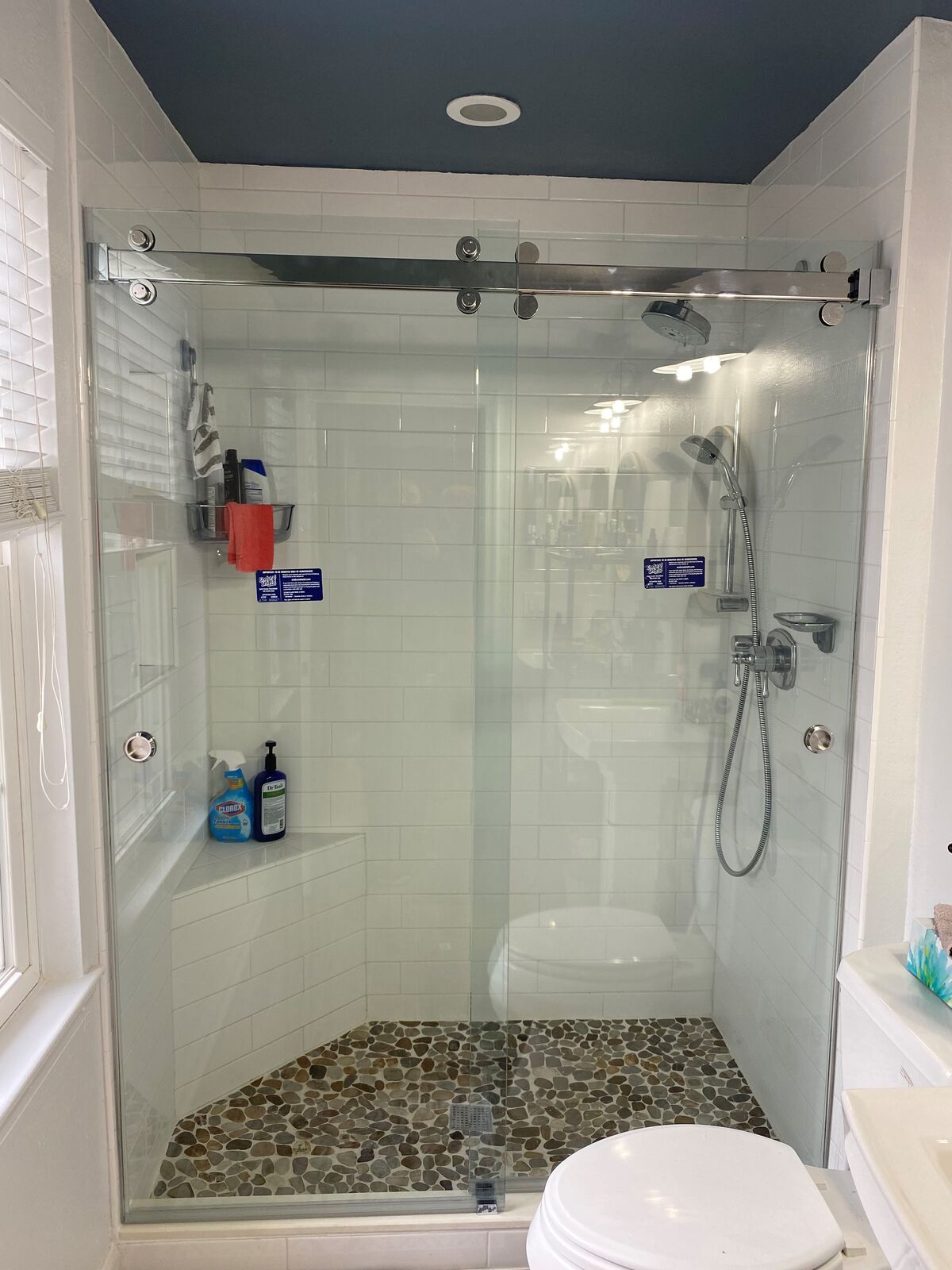 Sliding glass shower doors hanging from overhead rollers on a top bar