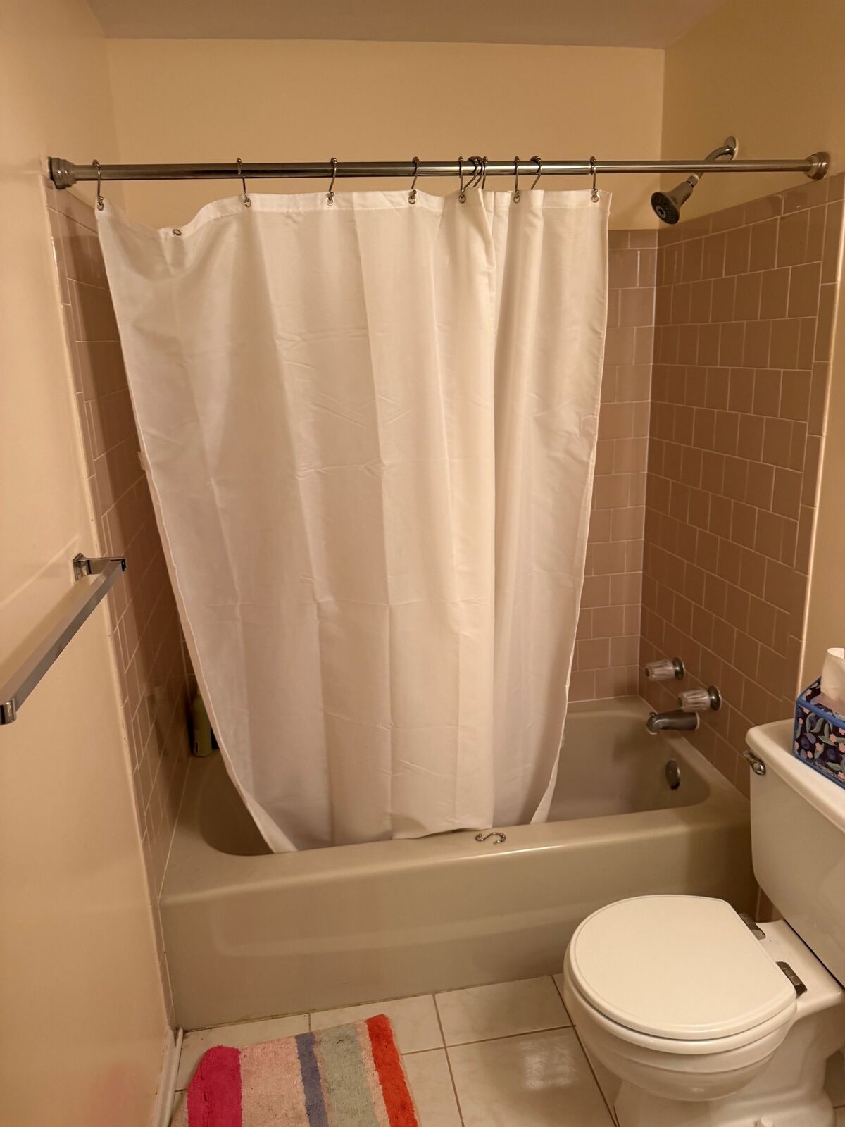 A bathtub with a plain shower curtain, before a glass enclosure is installed