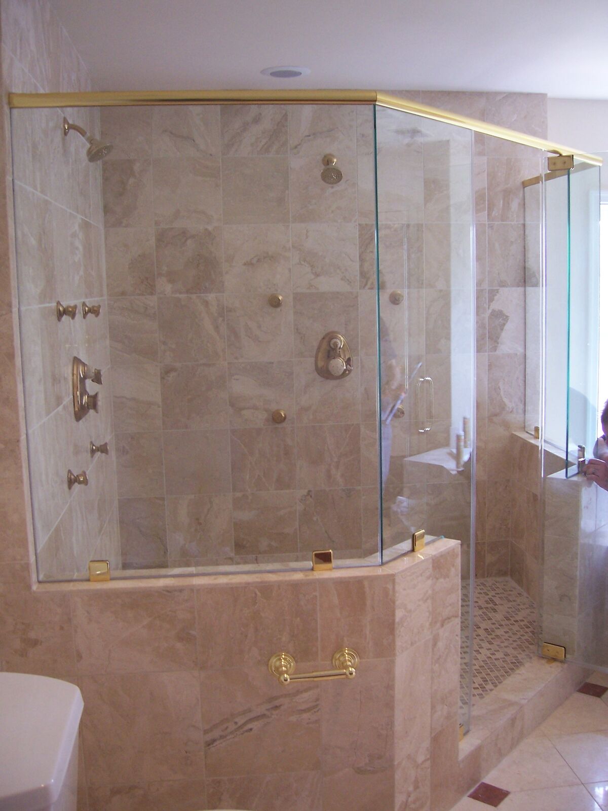 An angled glass shower enclosure sitting on tiled half walls with brass-tone trim