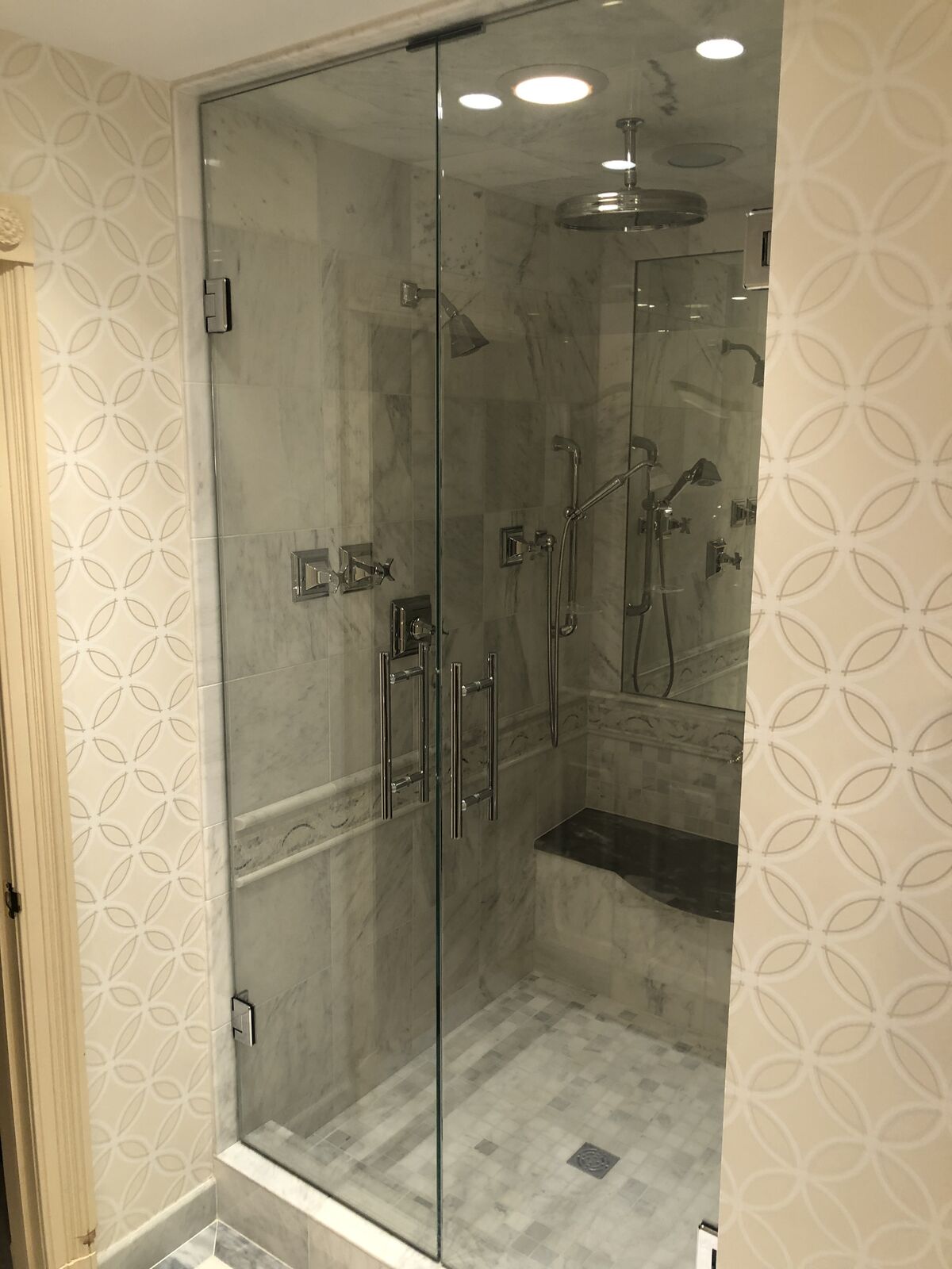 A floor-to-ceiling glass shower enclosure beside patterned wallpaper