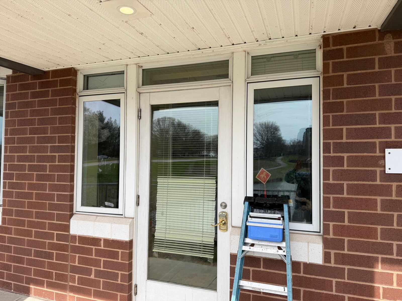 A commercial entry door with glass sidelights and a work ladder during installation