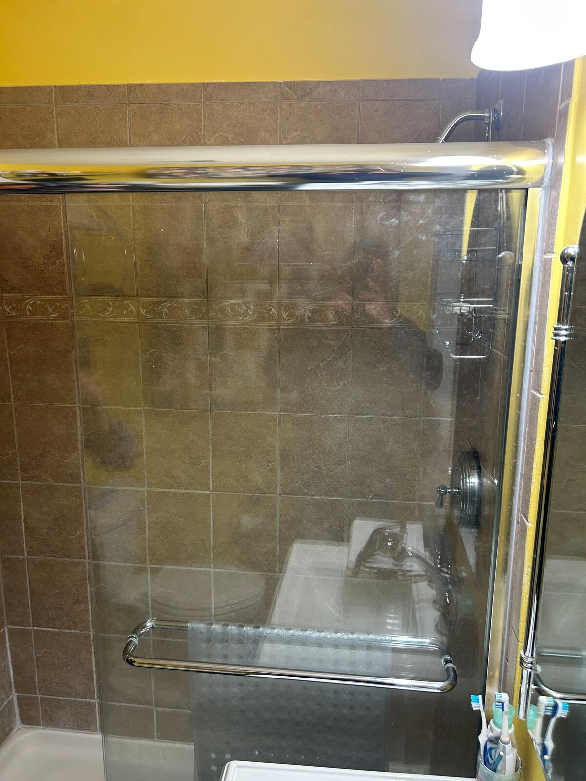 An older framed glass shower door in front of brown wall tile