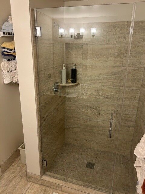 A clear frameless shower door in front of stone-look shower tile