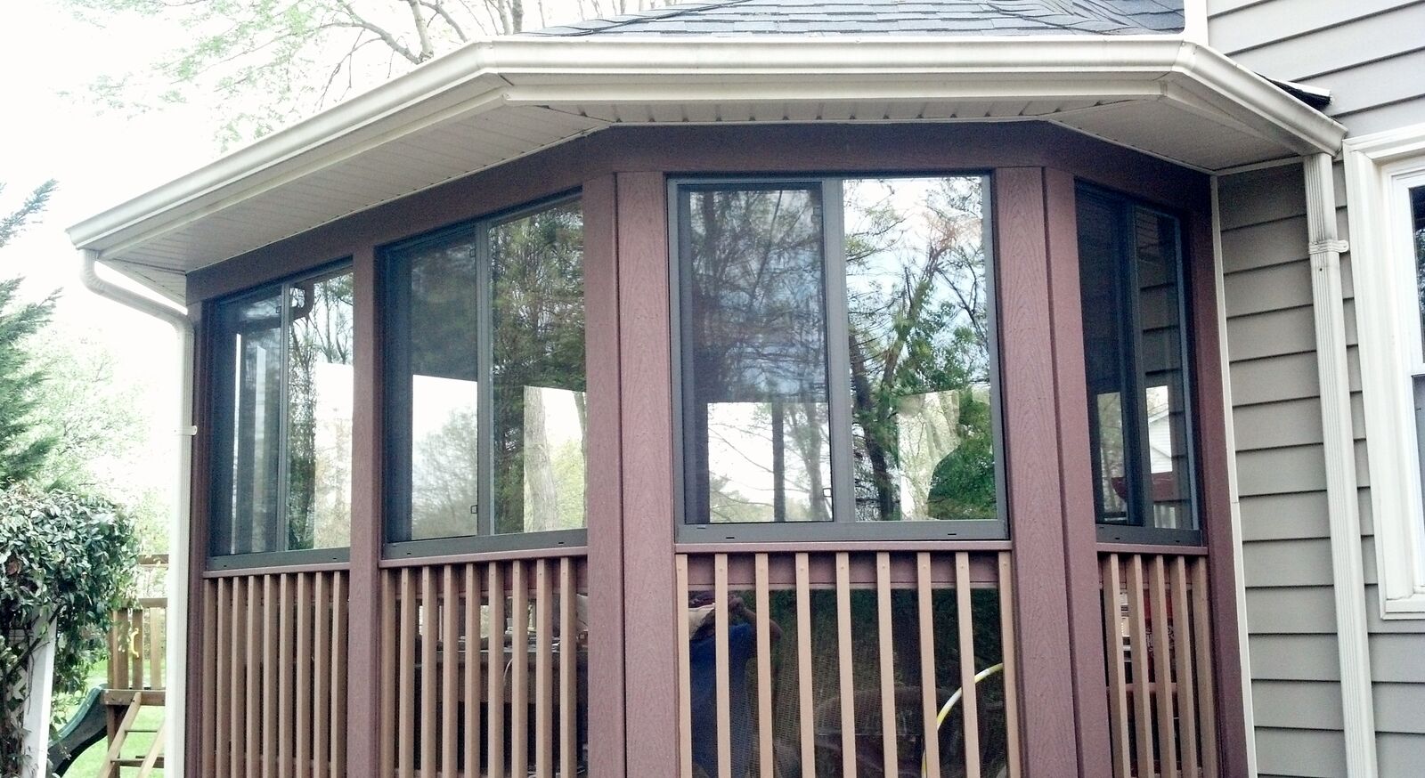 A porch with window panels in burgundy frames above vertical wood railings