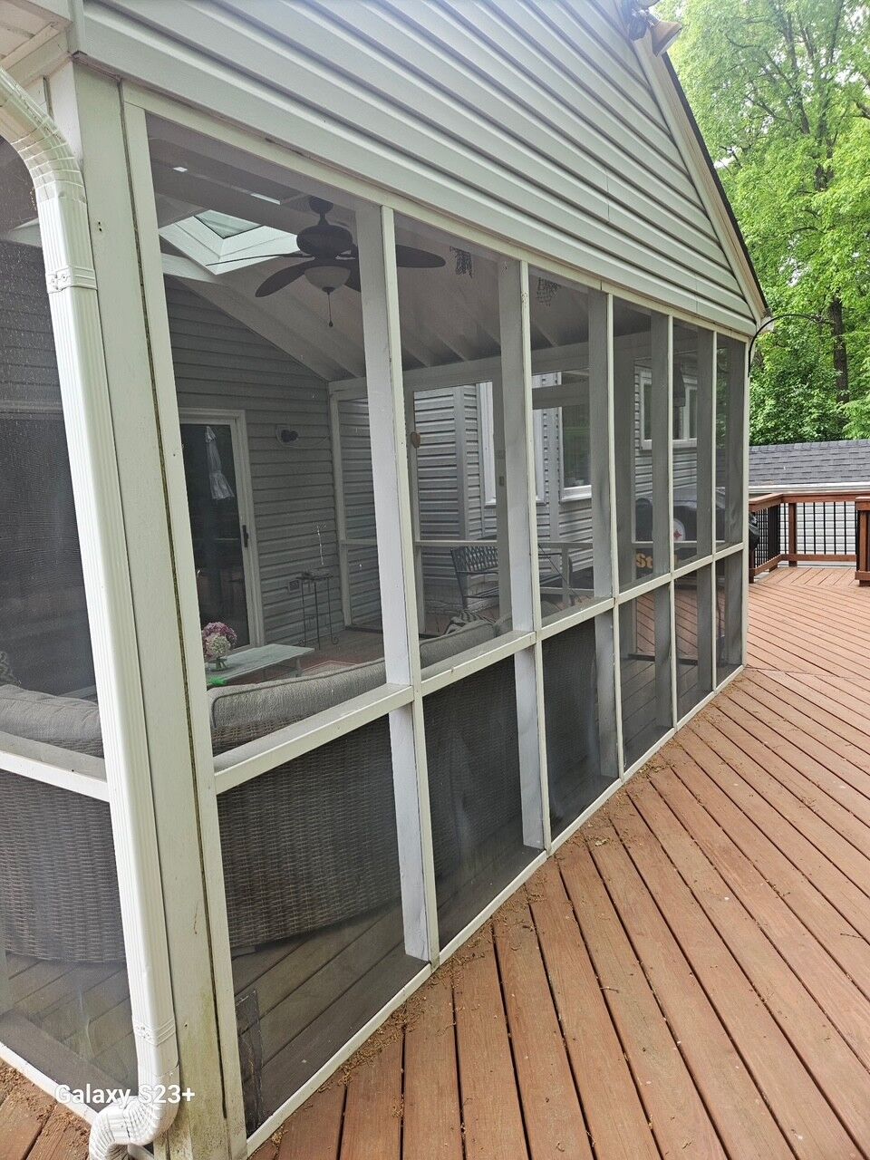 A screened porch on a wood deck with tall dark screen panels and white trim