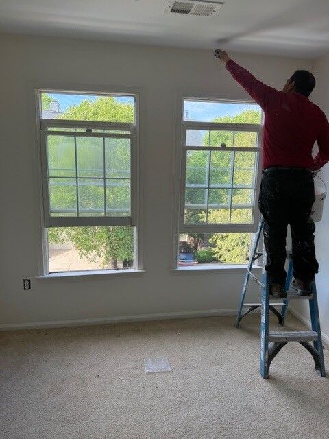 A technician on a stepladder working at a pair of bedroom windows