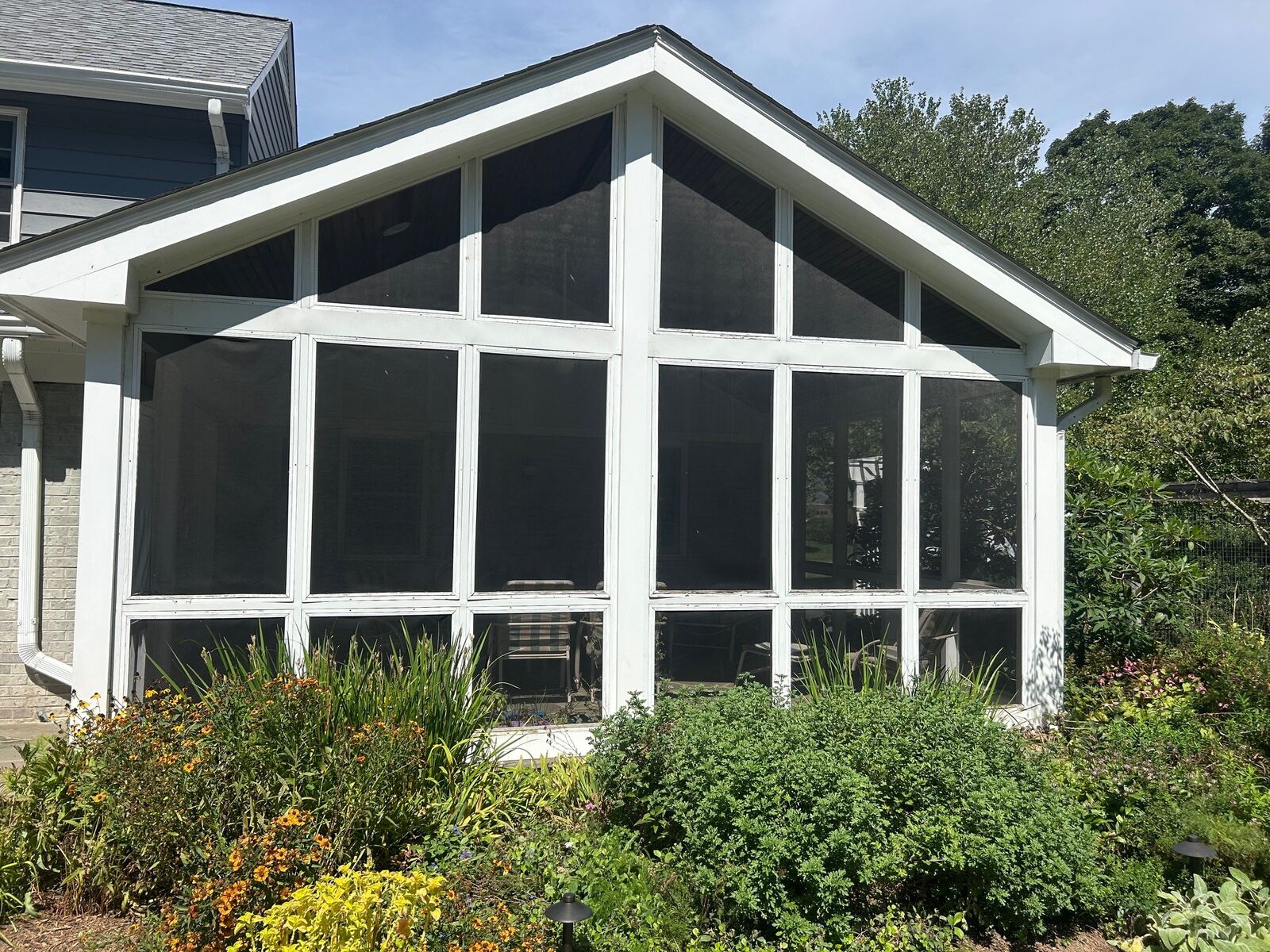A gabled screened porch with fresh dark screen panels, seen from the garden