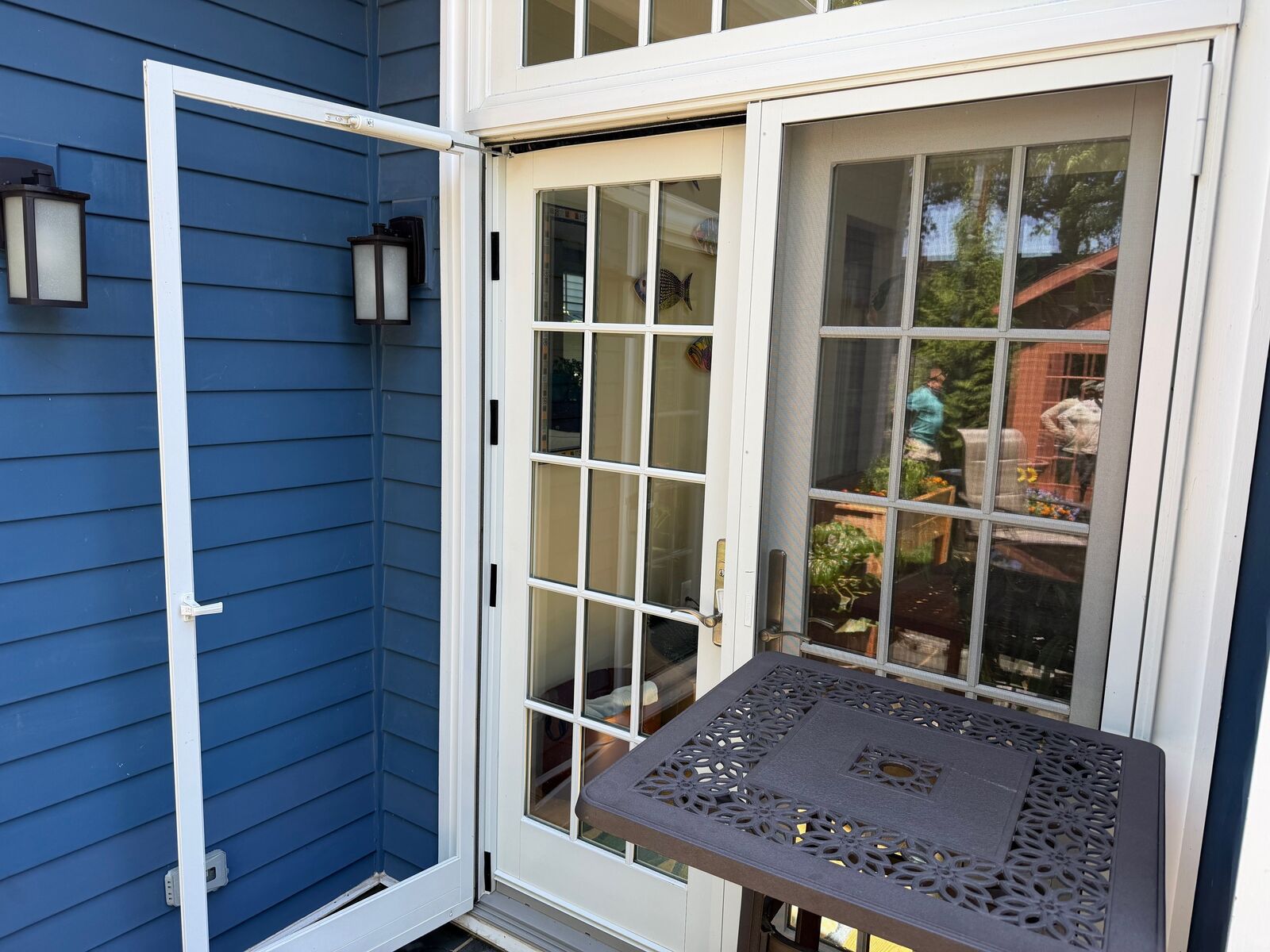 An exterior screen door standing open beside French doors