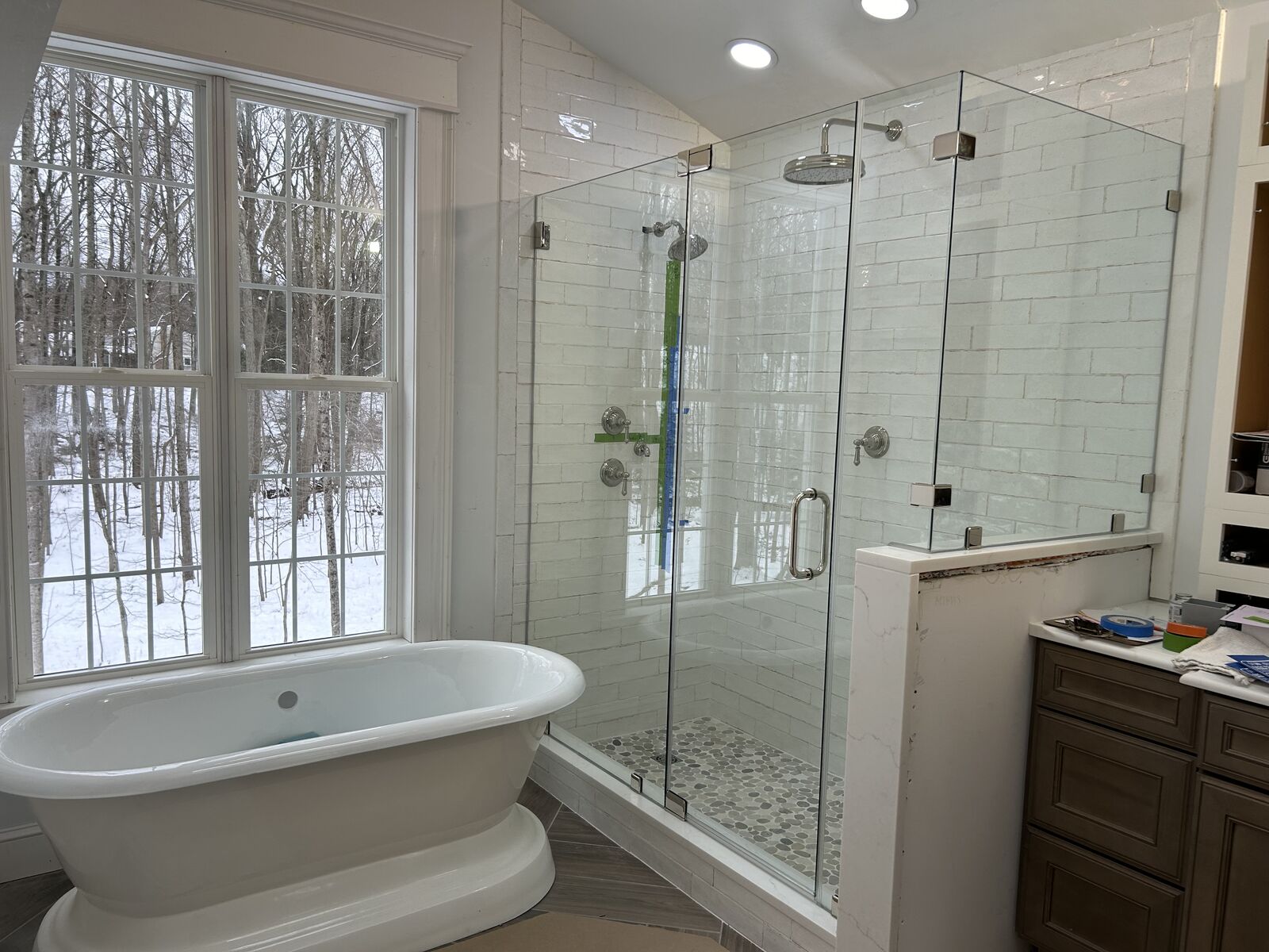 A frameless glass shower enclosure beside a freestanding tub and tall windows