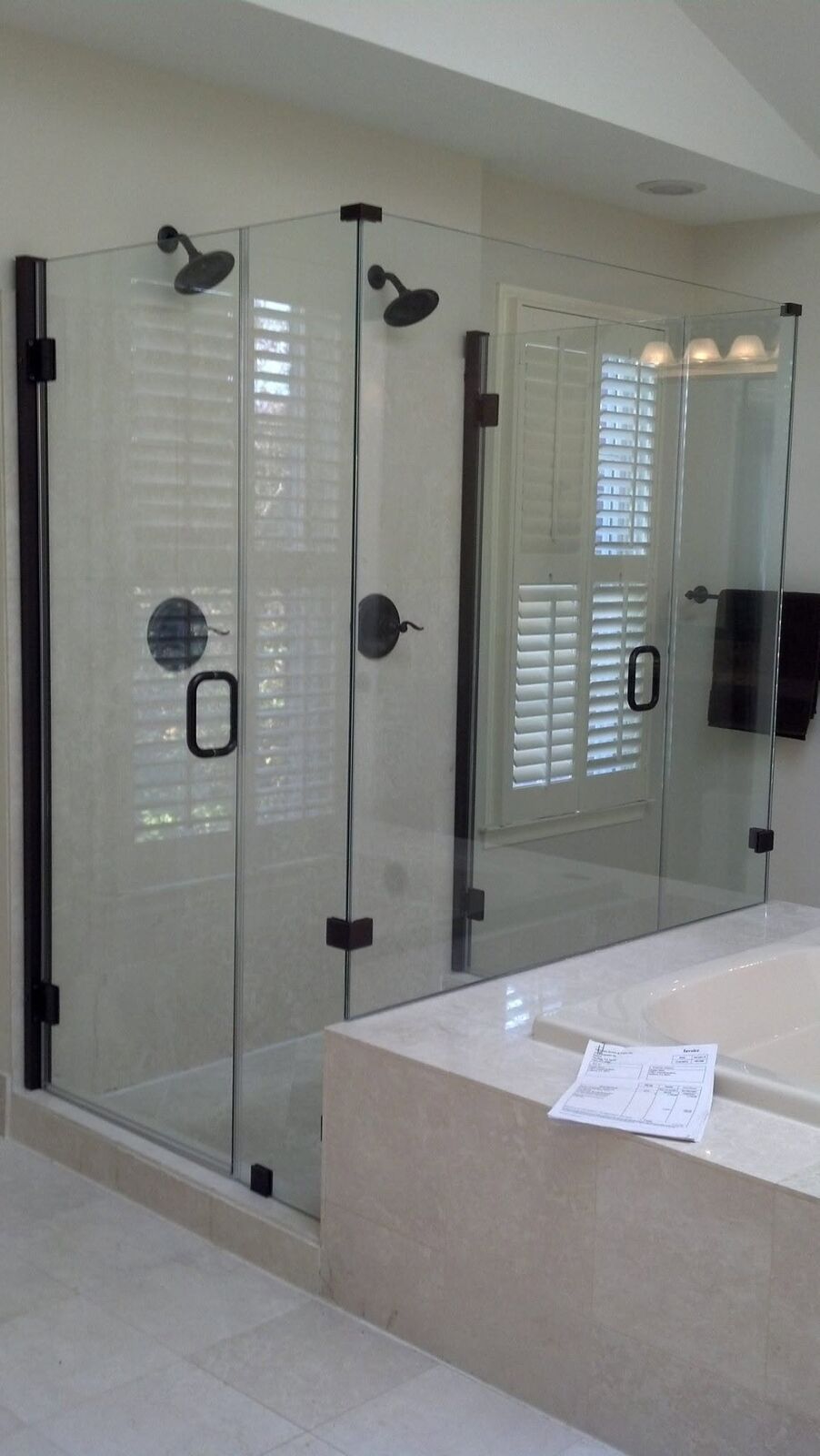 A frameless glass shower with matte black hinges and handle beside a tub deck