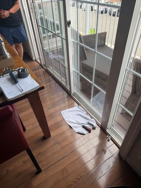 A patio door with grids seen from inside a room, with tools on the floor during a repair