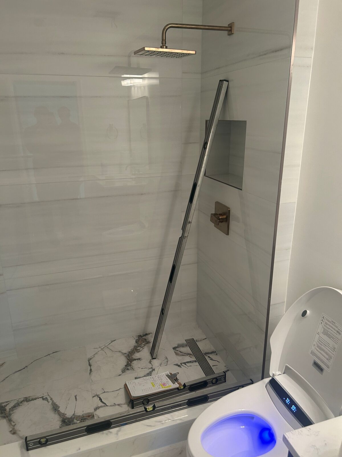A finished tiled shower opening with a rain head and a level leaning in the opening, before glass is installed