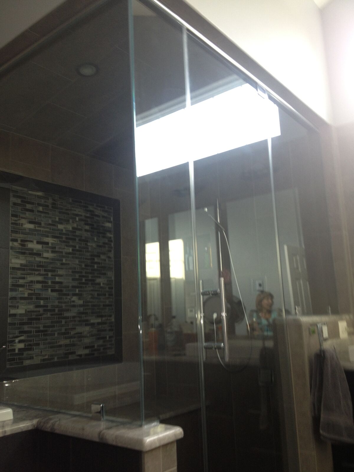 Tall shower glass with an upper transom panel near the ceiling and a mosaic accent wall