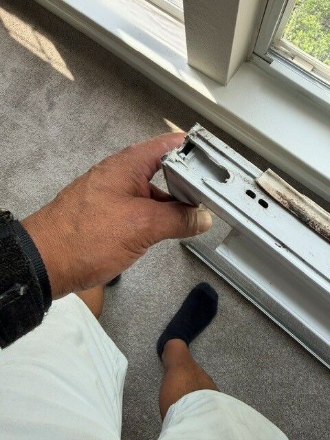 A hand holding a window sash hardware part beside an open sash